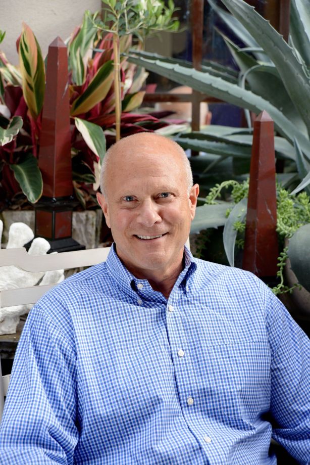 Man in blue shirt sitting on bench, smiling at camera.