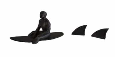 Bronze metal surfboard sculpture with two shark fins, depicting a surfer in action against a white background.