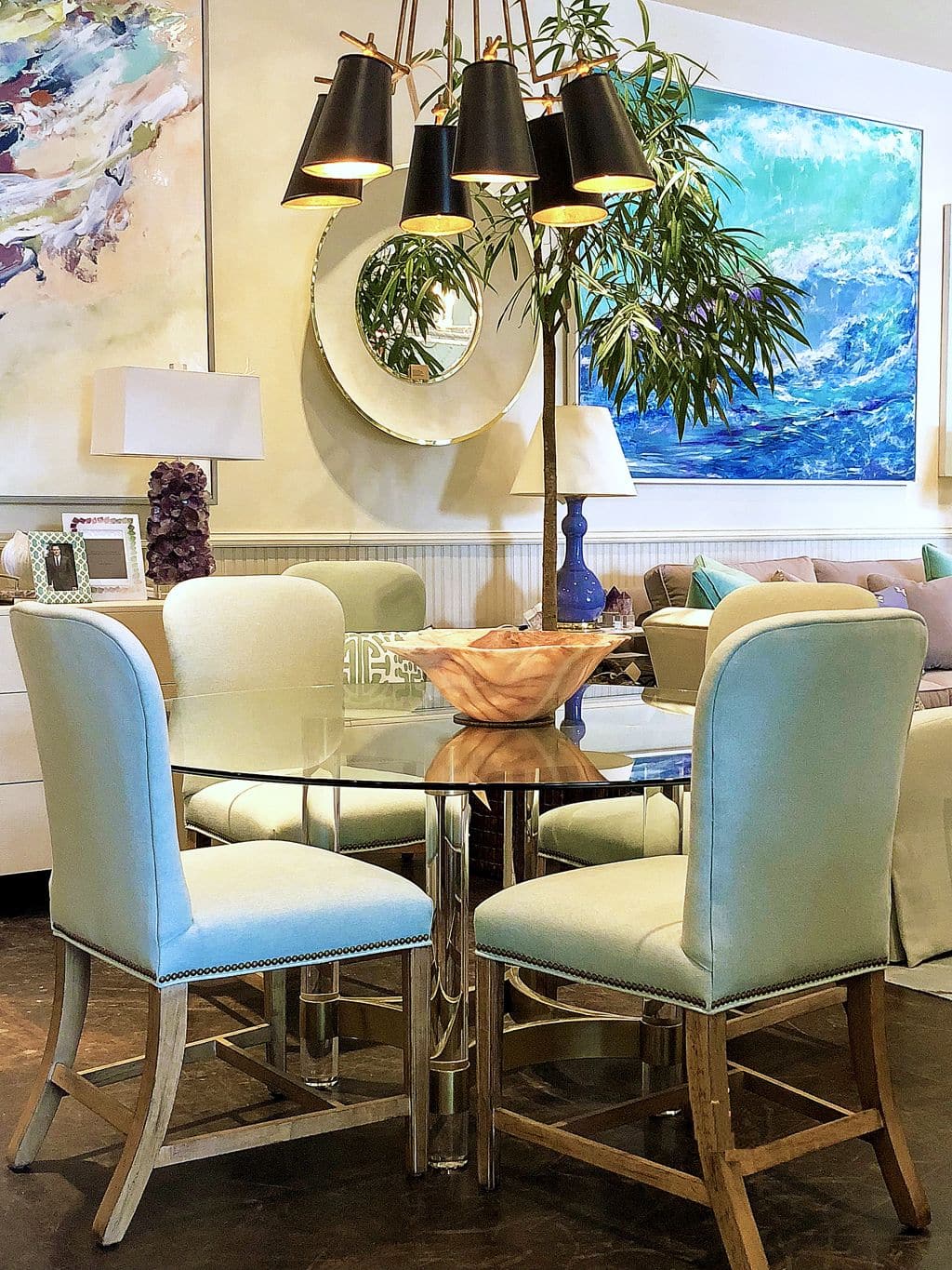 A modern dining room table with six chairs set against a wall with framed art and a large mirror The table has