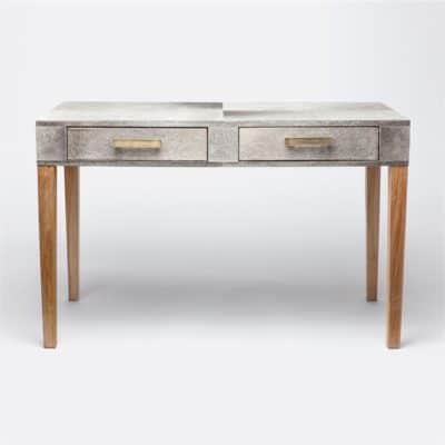 A Diane Desk with grey cowhide top and wooden legs. The desk has brass handles on its drawers.