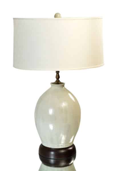 Matte white glazed ceramic egg lamp on wood base with cream linen shade.
