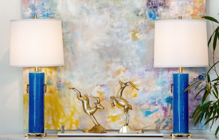 Blue and white ceramic lamp with brass base and rings, placed on a table near a wall.