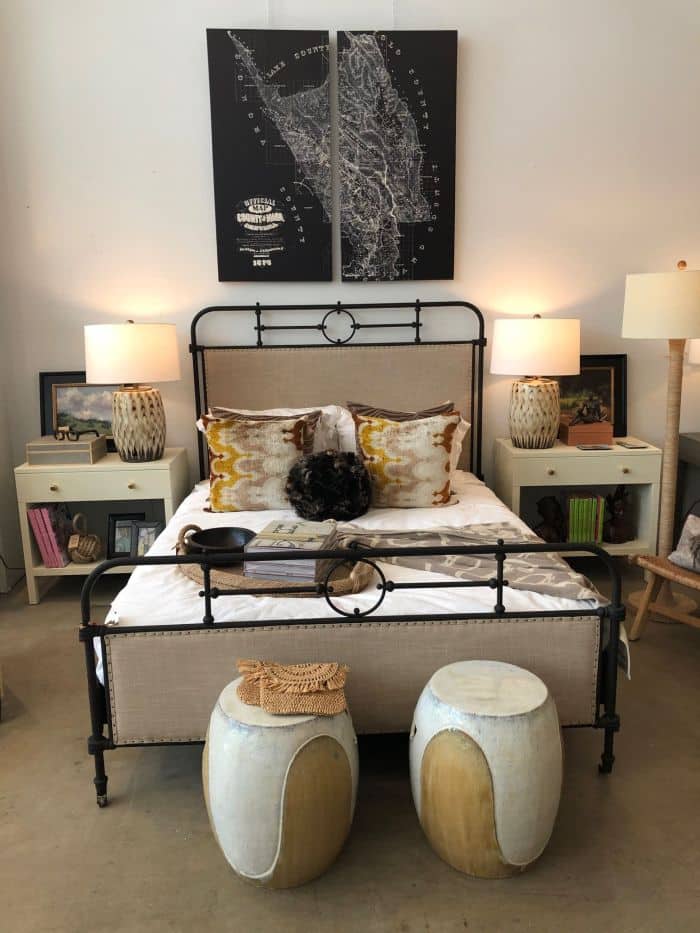 The room features a large bed adorned with colorful pillows and a wooden headboard flanked by two decorative stools A nightstand with