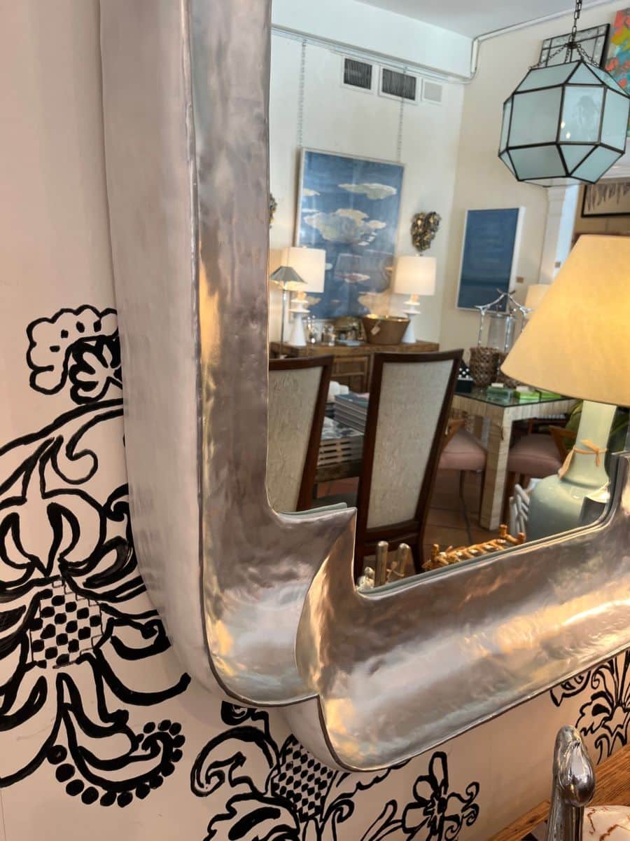Gold-trimmed small clipped corner mirror with decorative wallpaper behind.