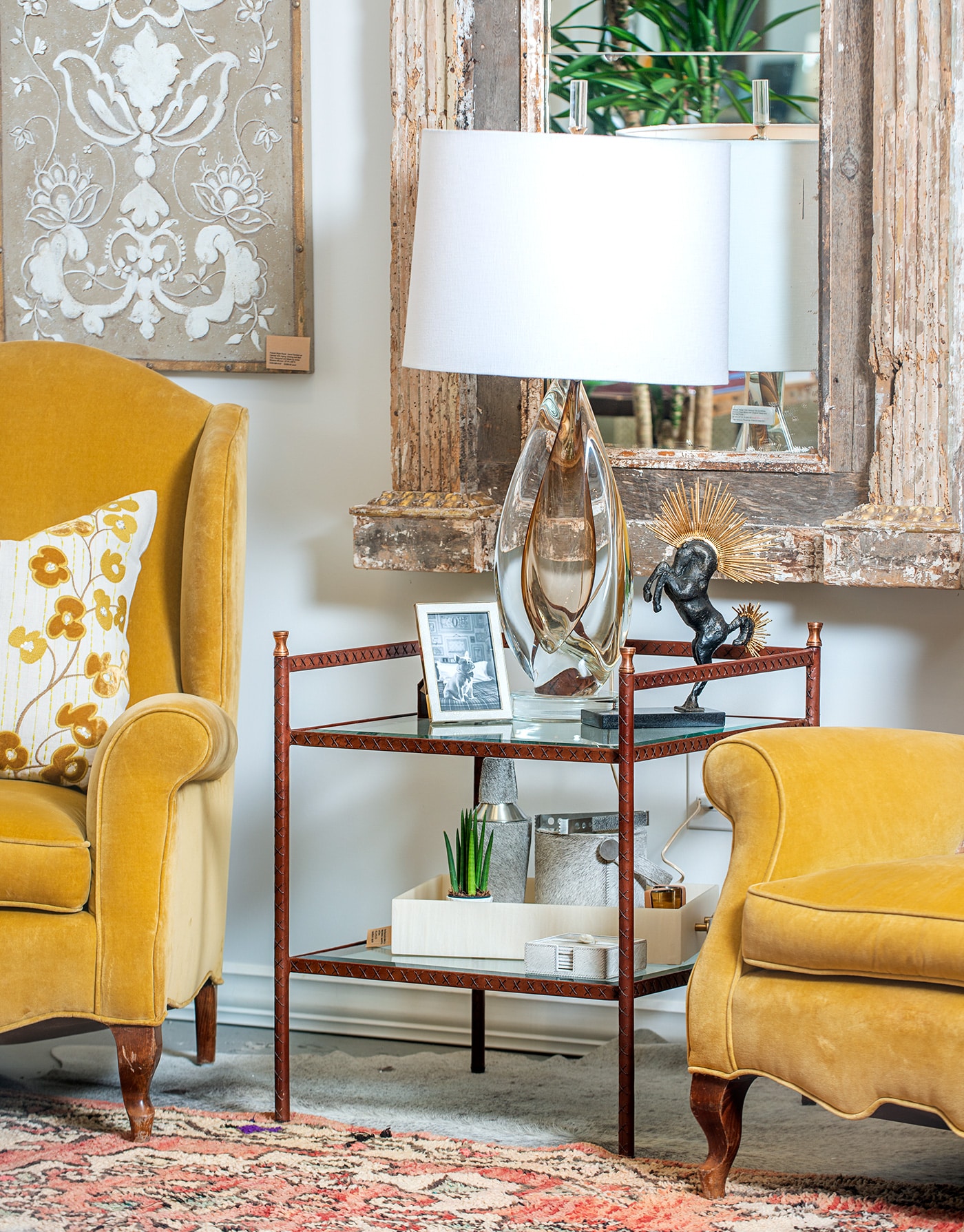 A stylish leather wrapped side table with glass shelves and brass finials, positioned against a wall in a living room setting.