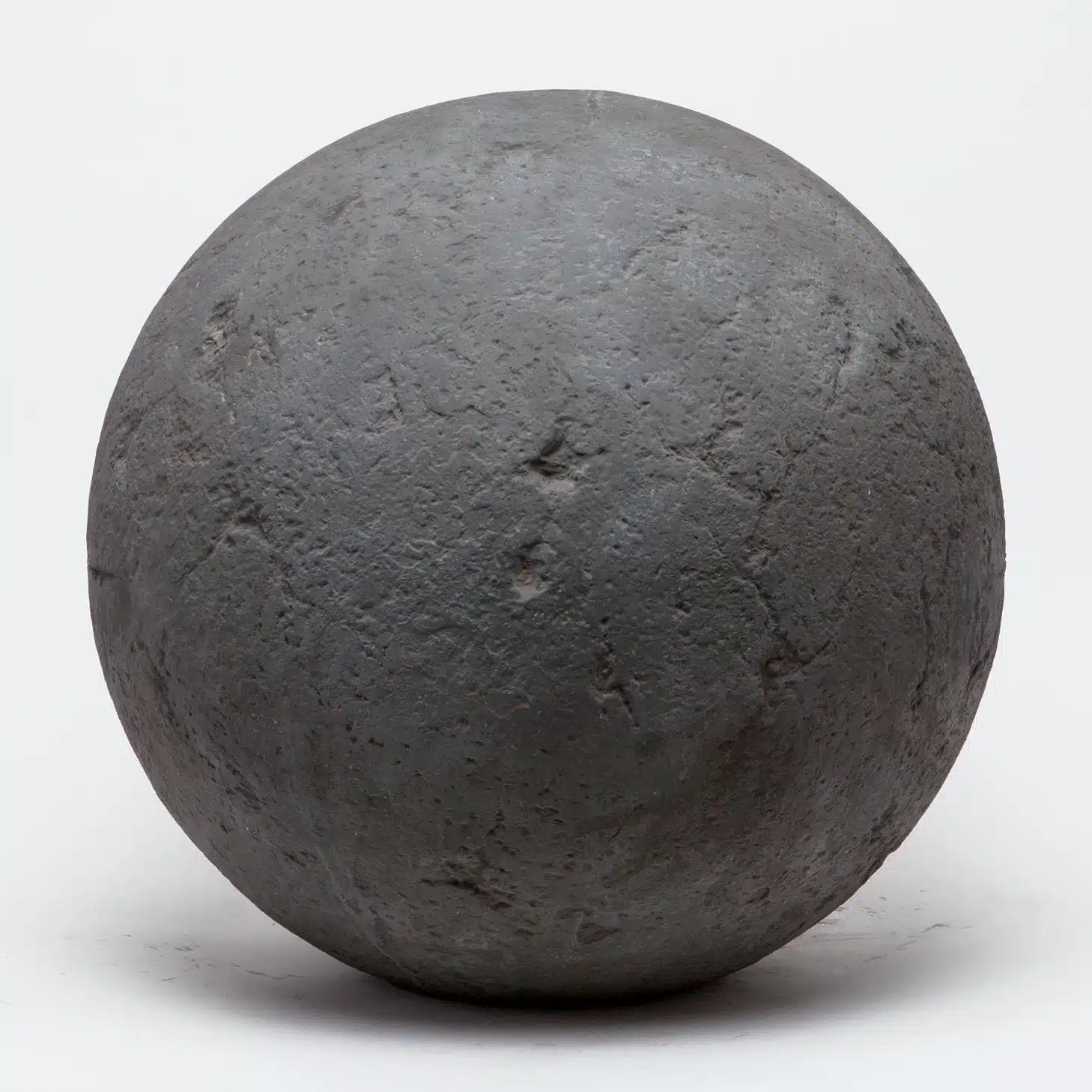 Oversized concrete ball in rough dark gray constituted stone, large spherical garden ornament.