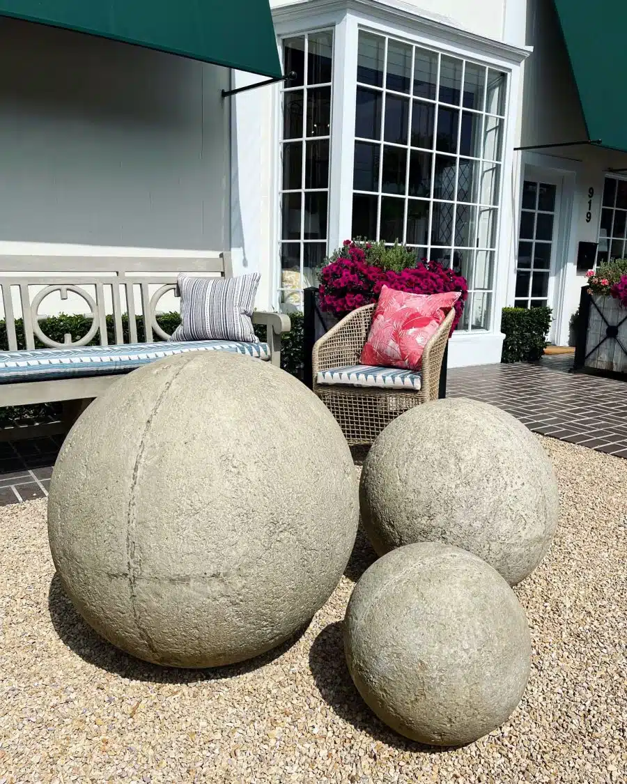 Oversized concrete balls in various sizes and shades of gray, sitting on gravel near a bench.