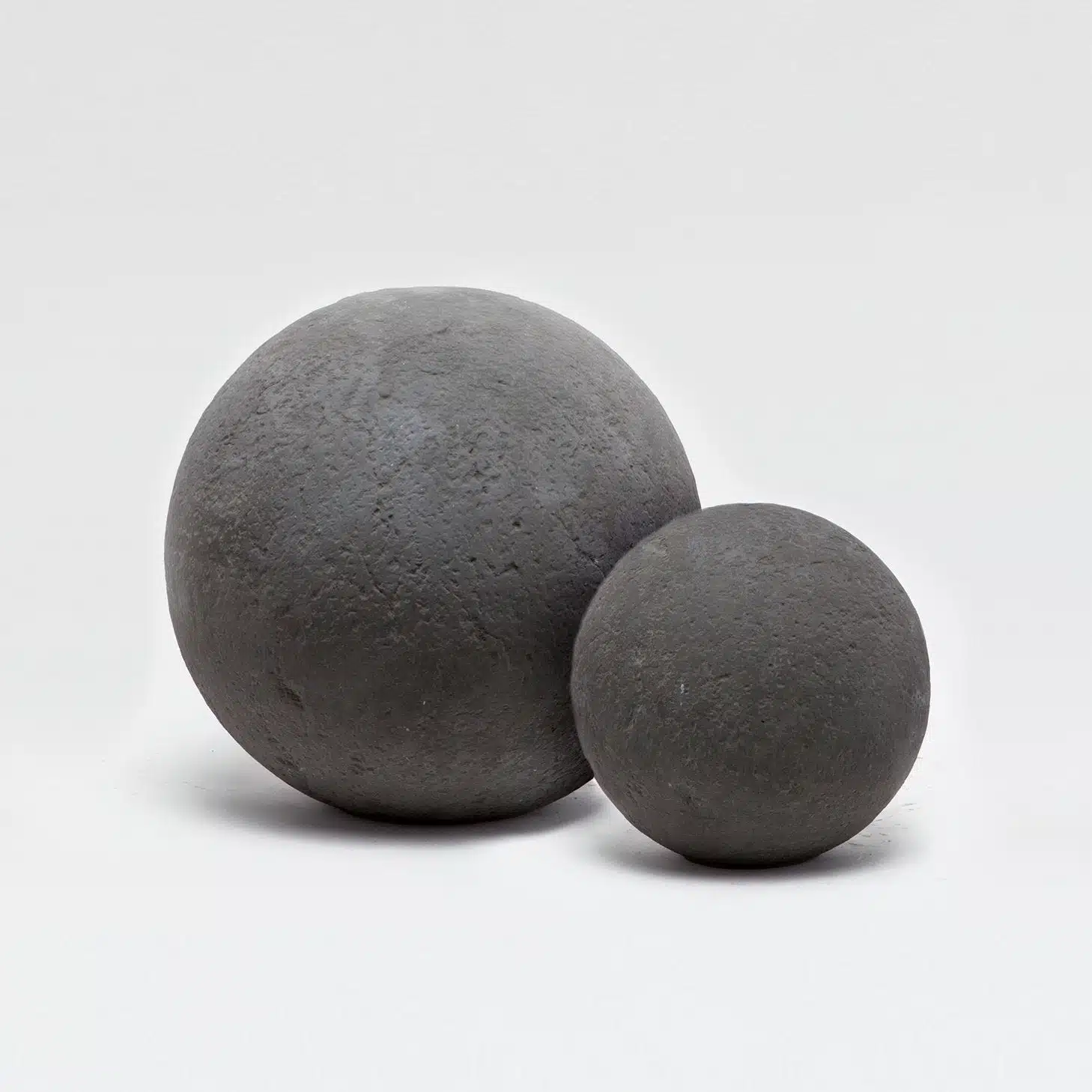 Large, rough dark gray concrete ball with a distressed light beige gray counterpart, showcasing spherical garden ornaments.