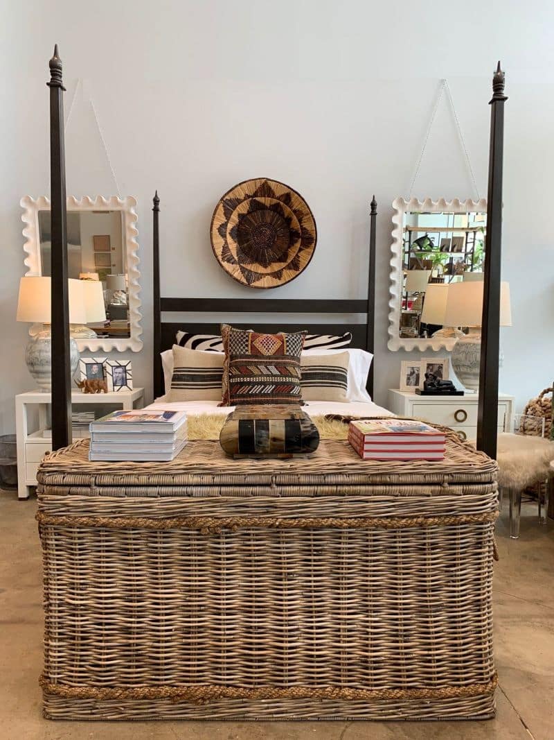 Antiqued white resin wave mirror with a bevel frame, displayed in a bedroom setting on a wicker table.