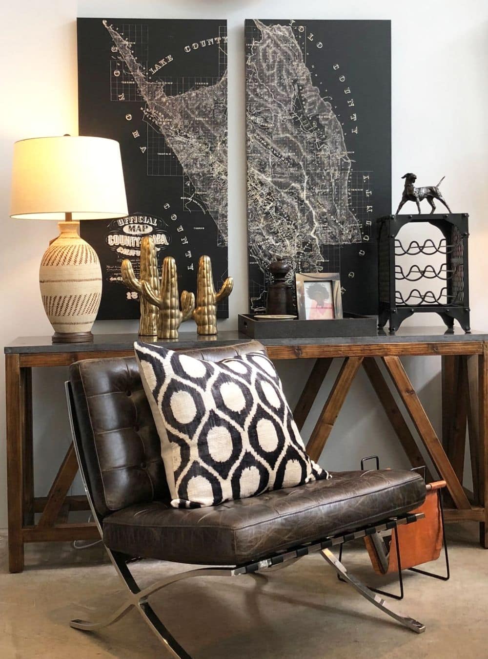 Iron and leather magazine rack in a room with two paintings on the wall, a couch, and a table.