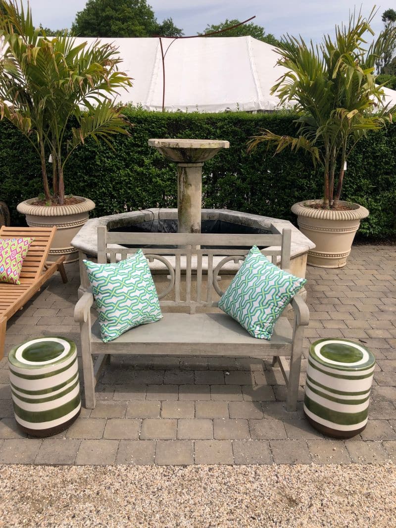 A blue and white striped ceramic stool in a garden setting, featuring two pillows on a bench behind it.