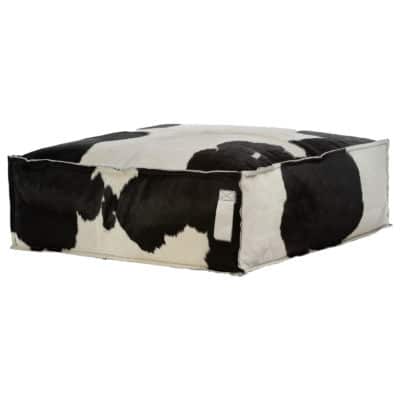 A black and white cowhide ottoman with a visible tag, placed on a white surface.