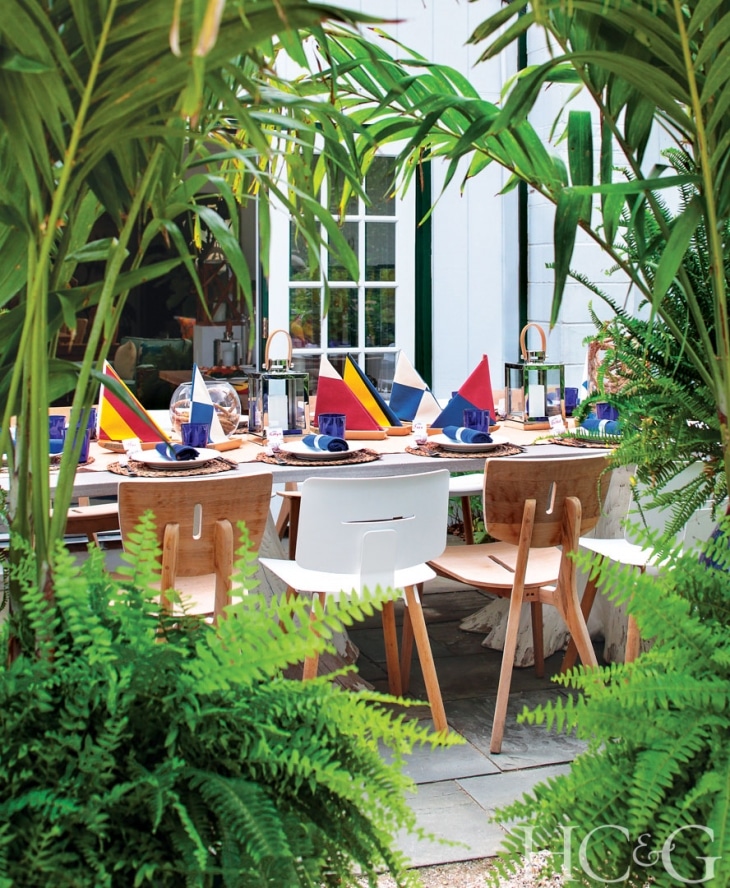 A table set for a nautical themed party, surrounded by tropical plants and a patio setting.