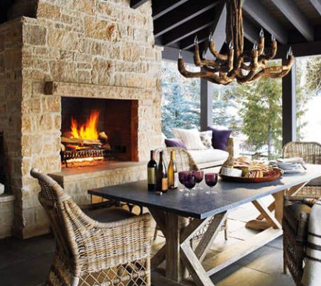 A cozy living room with a stone fireplace, a wooden dining table set for two, and a large window with natural light.