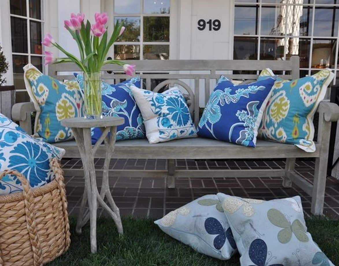 A bench with colorful pillows and a vase with flowers on a table in front of it set against a backdrop of