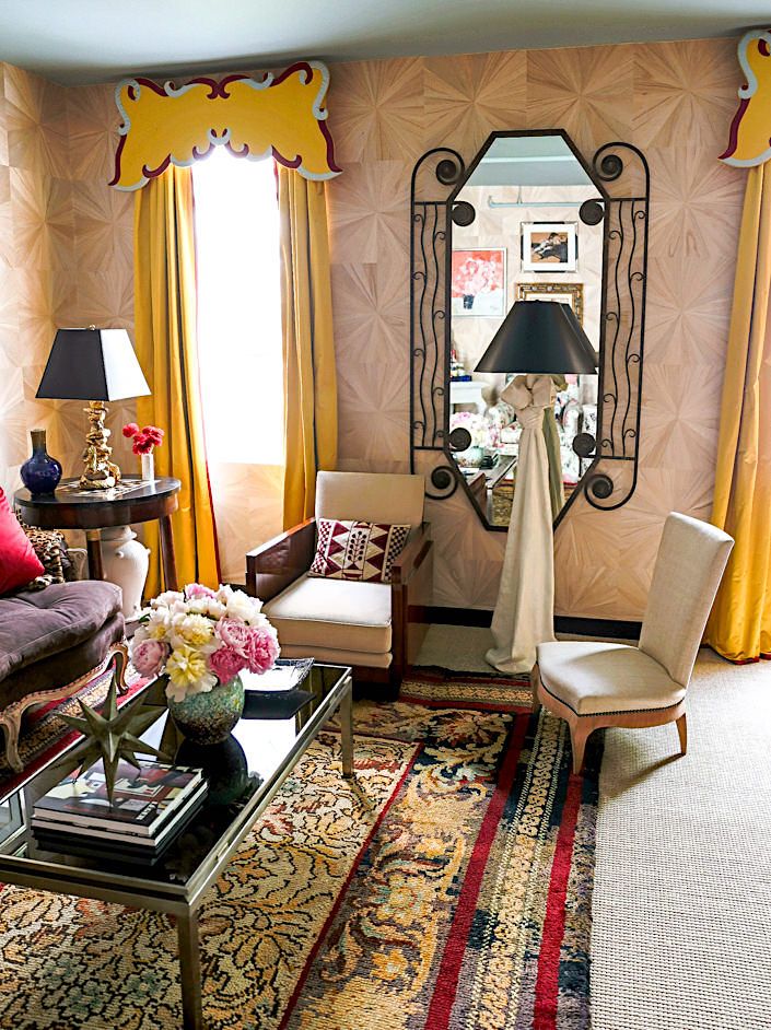 A well-decorated living room with a patterned wallpaper, a large mirror, a chandelier, a couch, and a table.