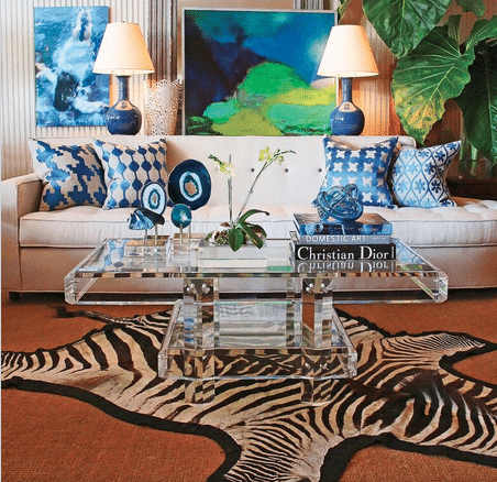 A luxurious living room with a large white couch adorned with blue and green pillows a glass coffee table in the center