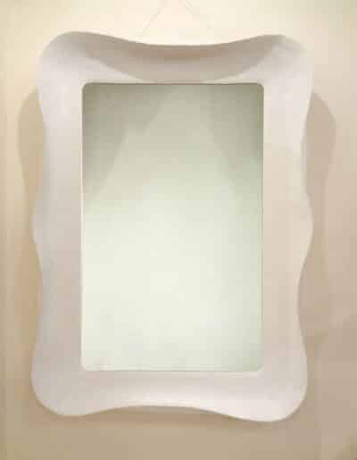 Small white modern wave mirror with a square frame, displayed on a wall.