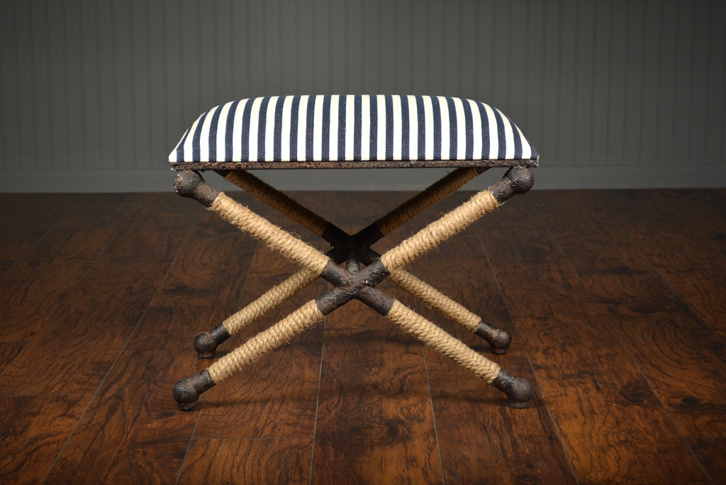 Black and white striped ottoman with a rustic iron frame, set against a wooden floor in a room with a dark wall.