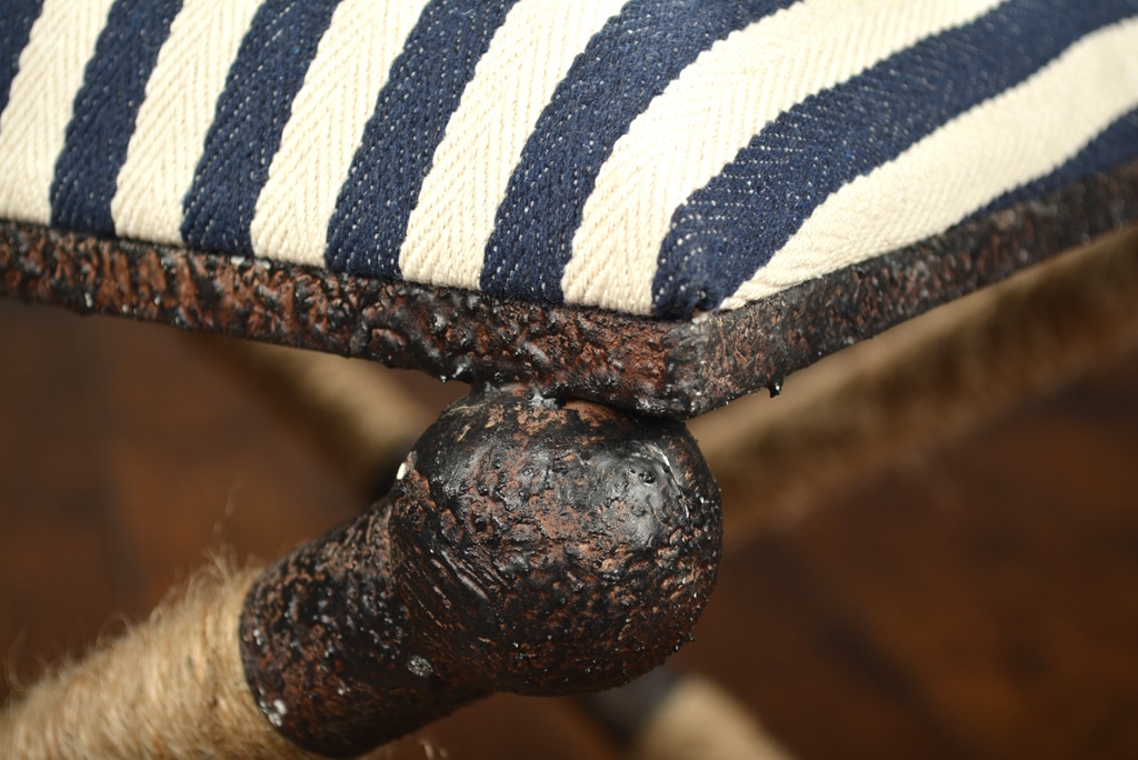 Small navy and white striped ottoman with a rope X design featuring a rustic iron frame and a visible knot in the