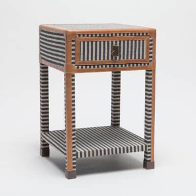 A small wooden nightstand with a navy and cream canvas stripe design featuring a single drawer and bottom shelf set against a