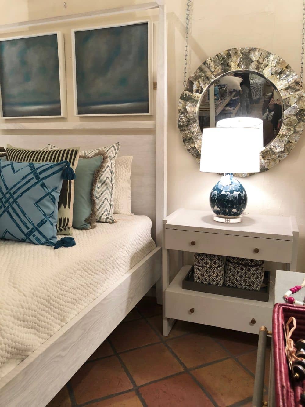 Large white nightstand with a blue vase on top in front of a bed with a blue and white patterned pillow and