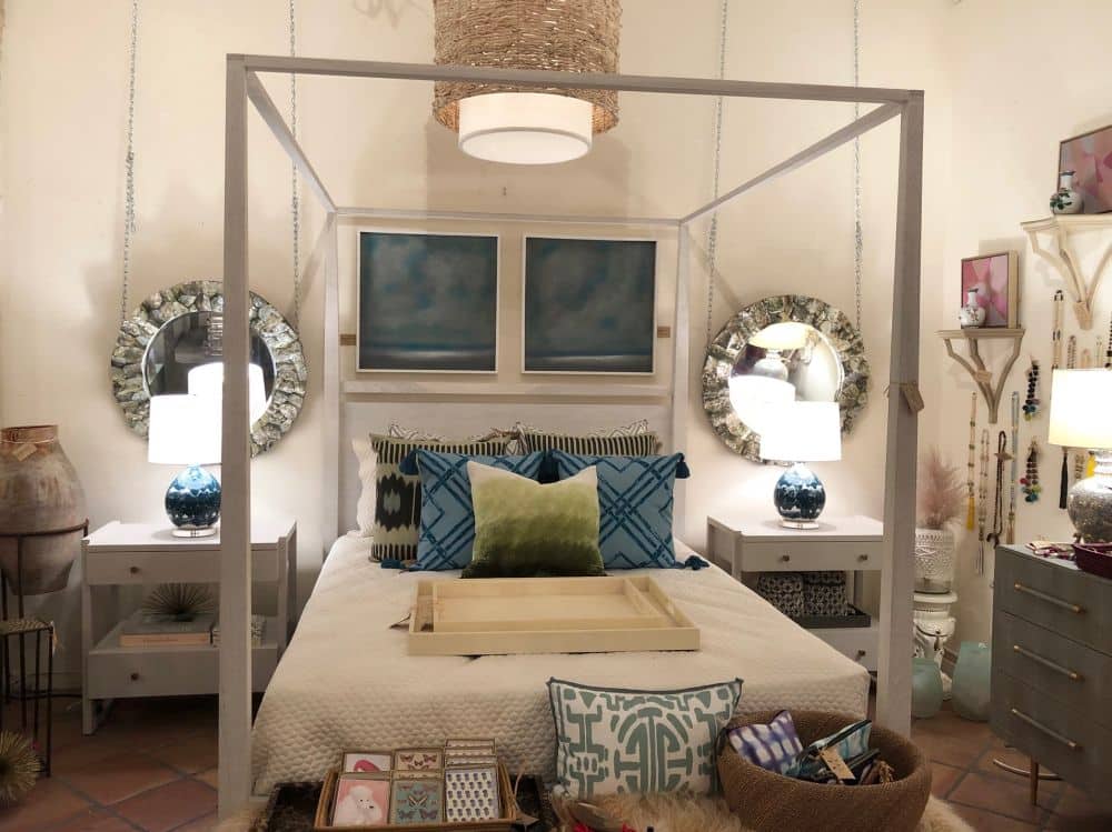 A large bed with a white frame and a blue and green throw pillow at the foot flanked by two nightstands with
