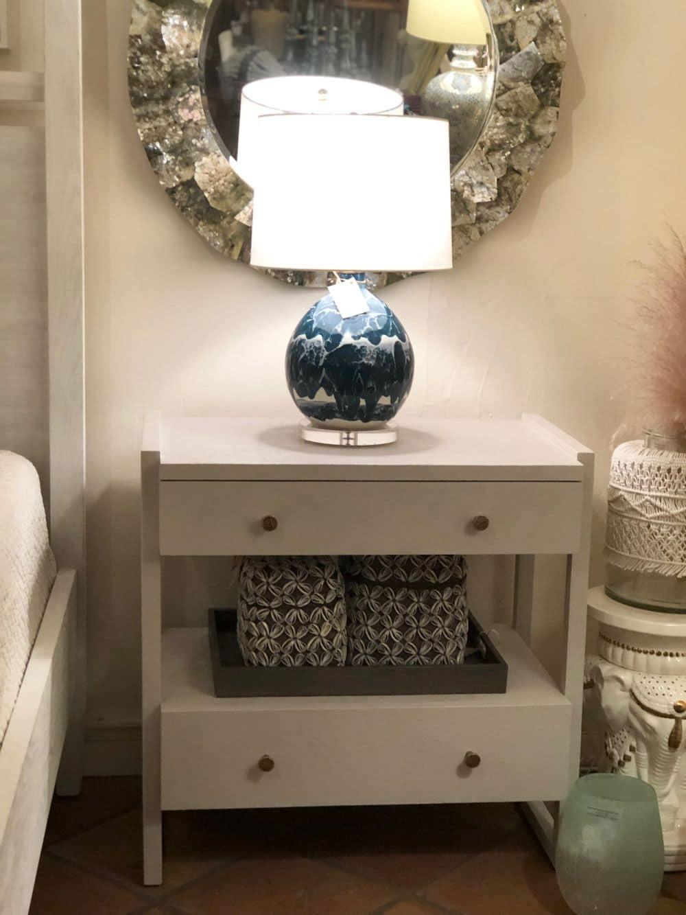 Large white nightstand with a blue vase on top, placed next to a mirror in a room.