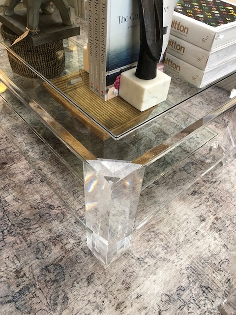 A clear glass and acrylic coffee table with a bottom shelf showcasing a few books and a small decorative item placed on