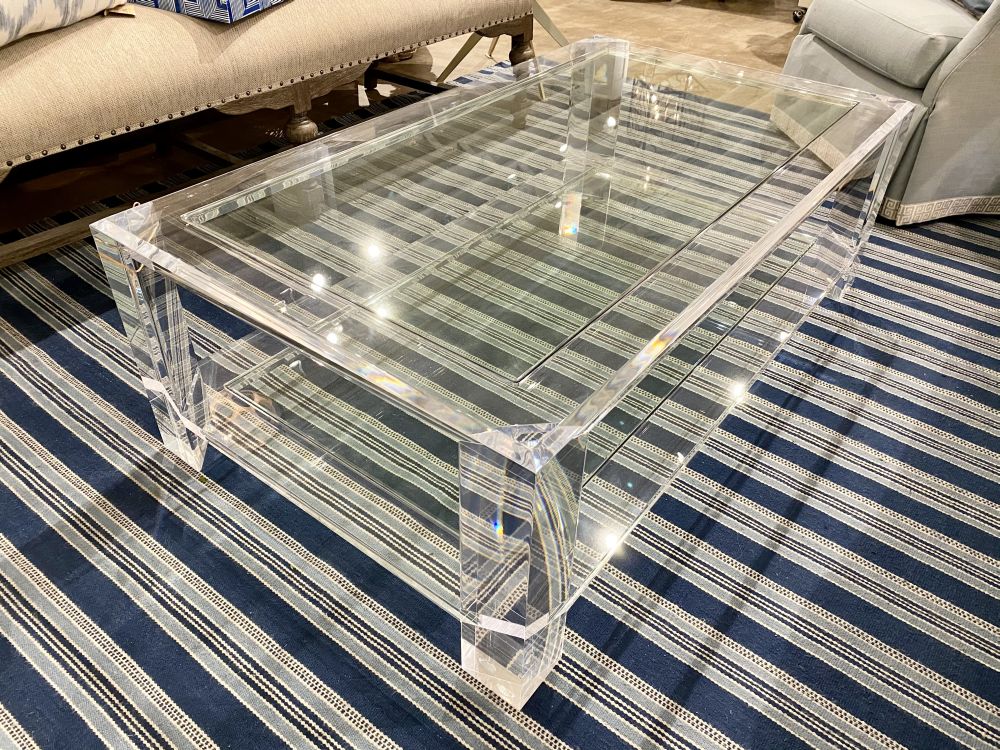 The Munson Acrylic Coffee Table is a sleek piece of furniture with a transparent acrylic top and bottom glass shelf supported by