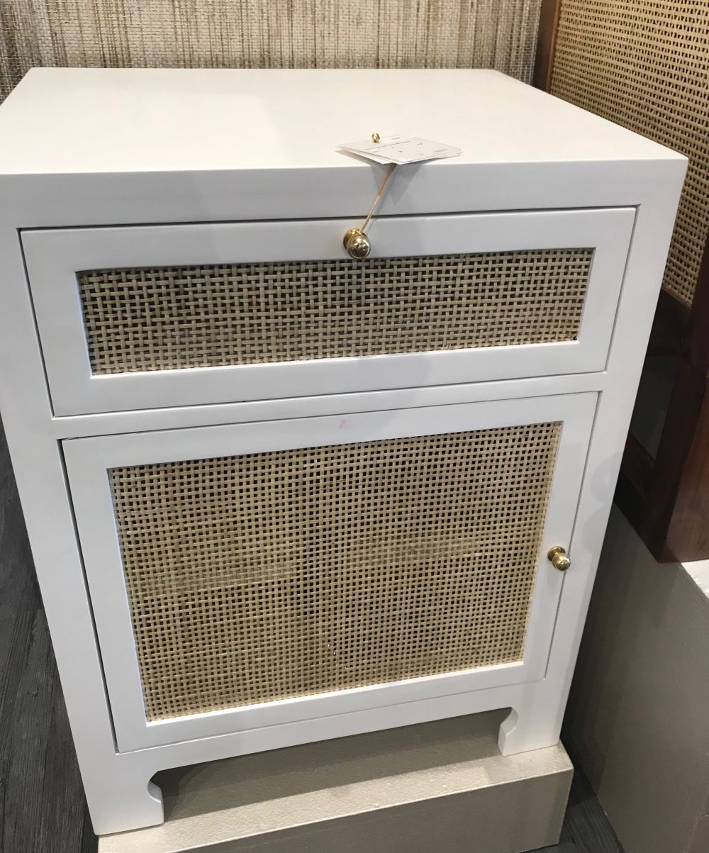 Small white lacquered cane front cabinet with one door and top drawer, set against a beige wall.