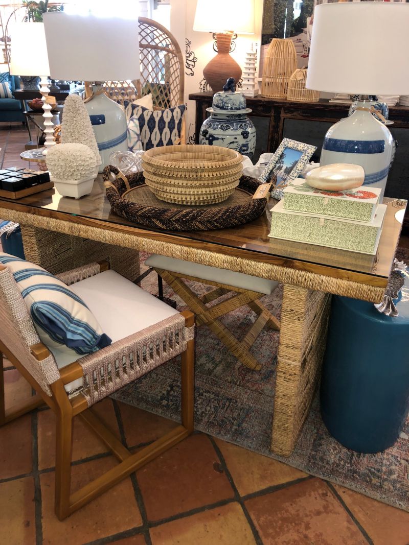 A luxurious woven base desk with a teak top, surrounded by various decorative items and furniture pieces.