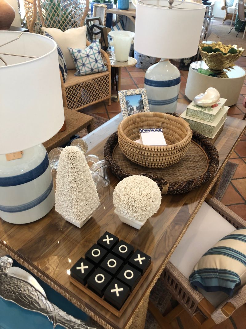 A large wooden desk with a woven base and a teak top displayed in a store alongside other home decor items such