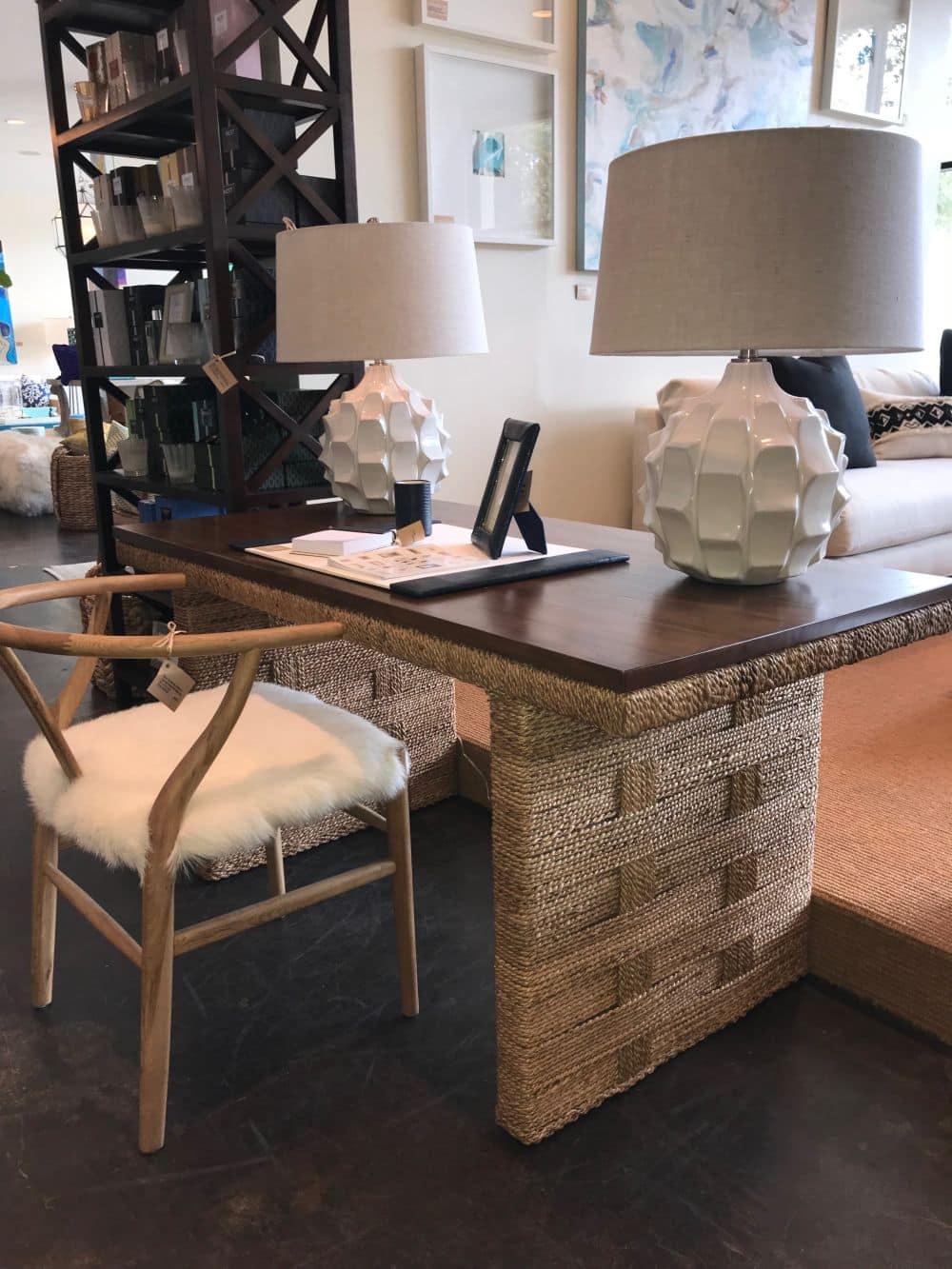 A woven and teak desk with a glass top, flanked by two chairs in a room with a modern decor style.