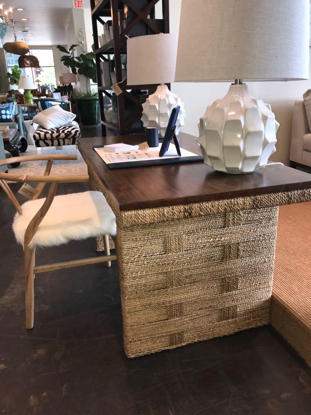 A woven and teak desk with a glass top shown in various locations including Hamptons Palm Beach Dallas Los Angeles and East