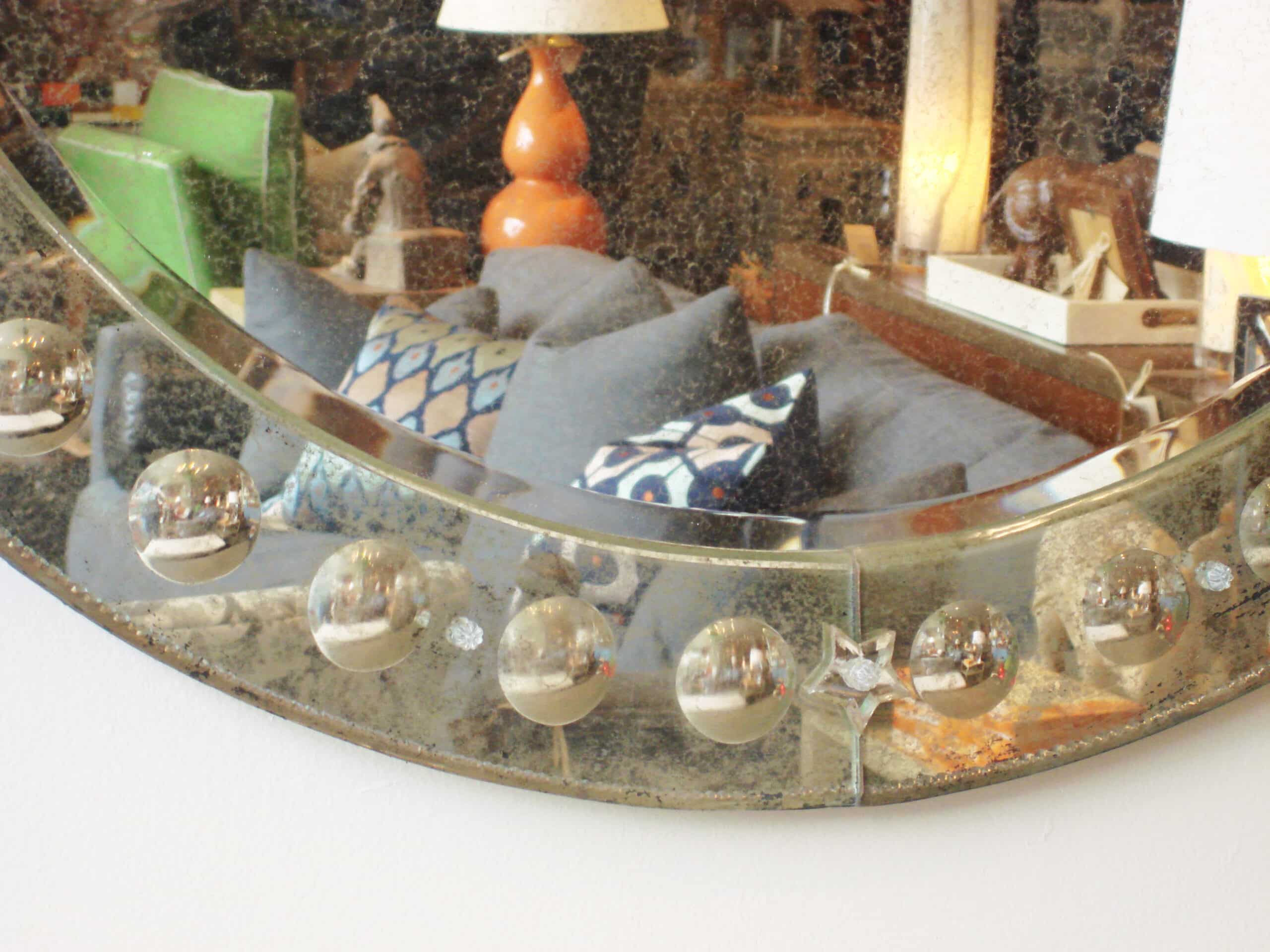 A large round antiqued Venetian bubble frame mirror with multiple spherical ornaments on a white background displayed in a room with a