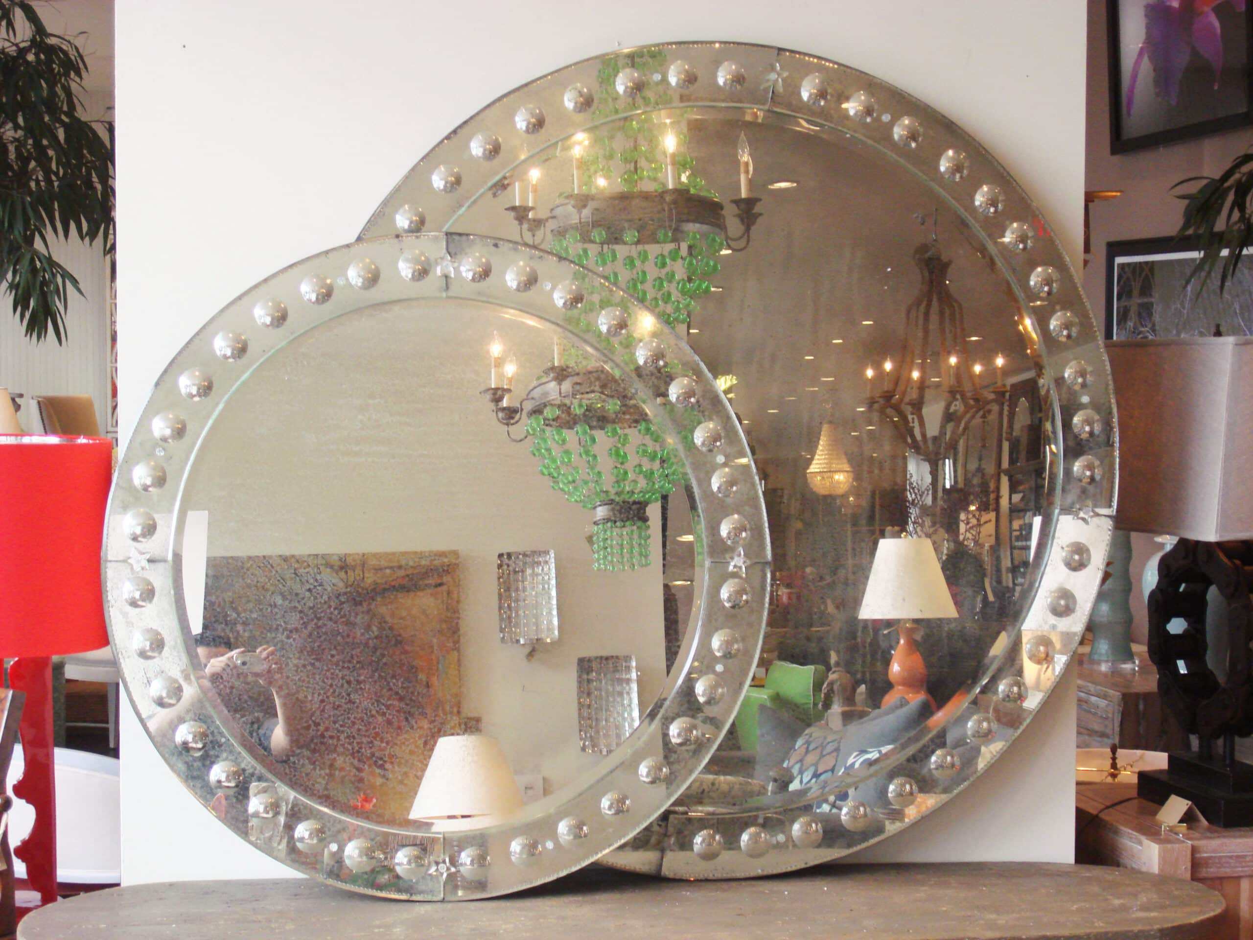 Large round antiqued Venetian bubble frame mirror with a shiny silver finish, displayed in a store.