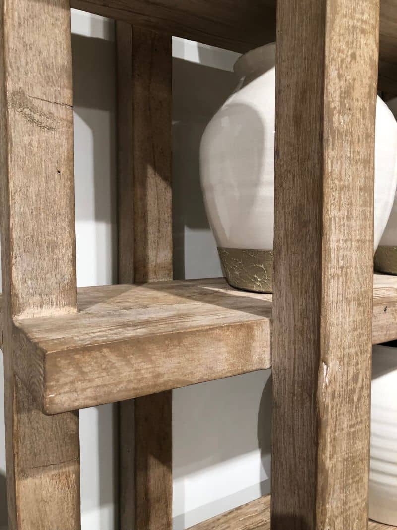 A wooden bookcase with a light wash finish, standing against a white wall.