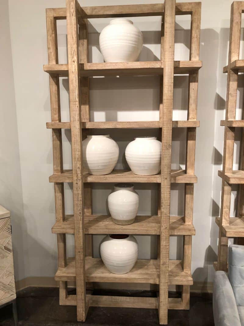 A wooden bookcase with three shelves, each holding a vase.