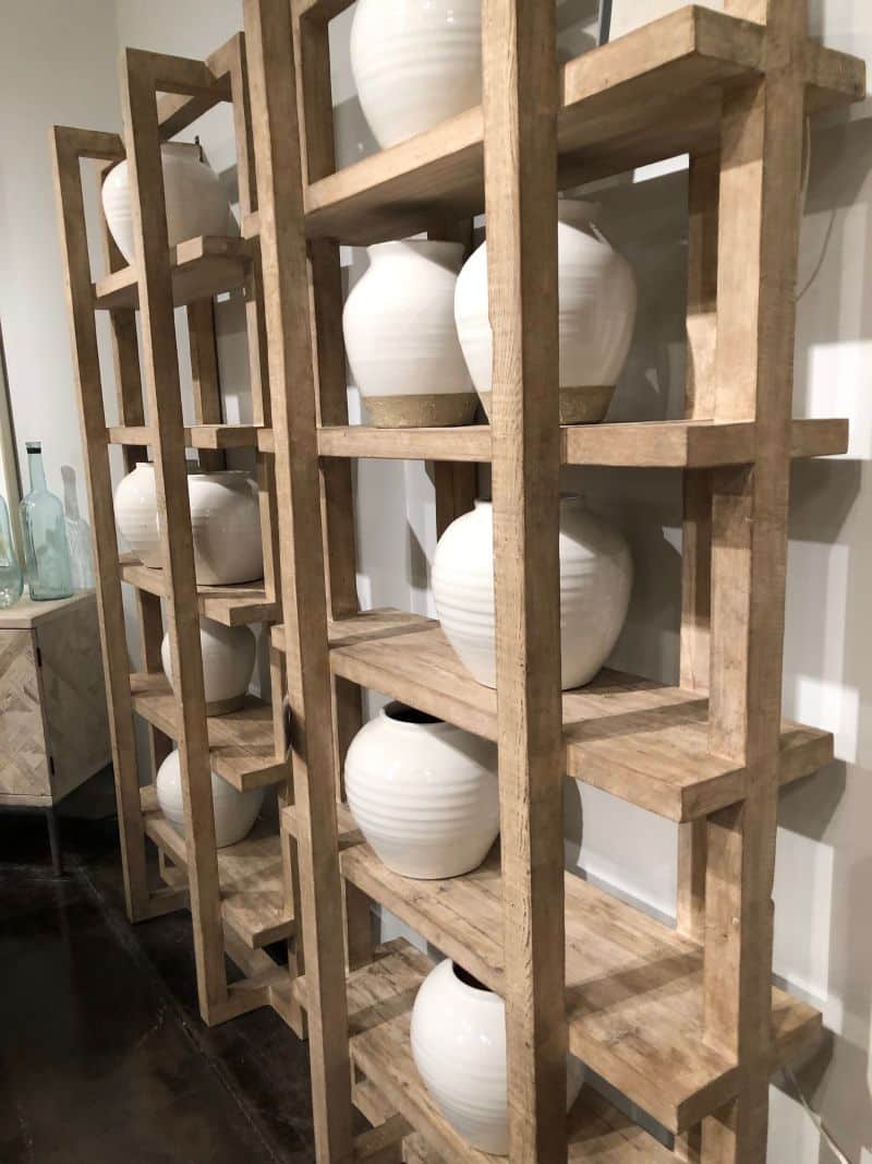A wooden bookcase with multiple shelves, each holding a vase.