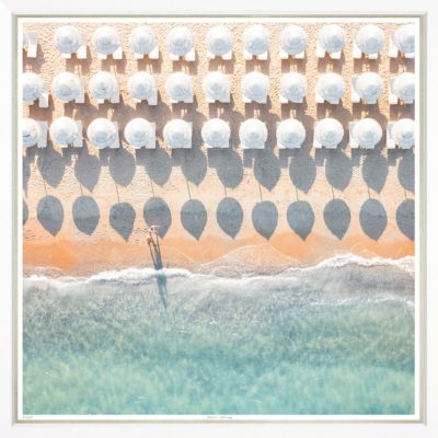The image depicts a beach scene with numerous umbrellas and chairs arranged in neat rows suggesting an organized resort or beach club