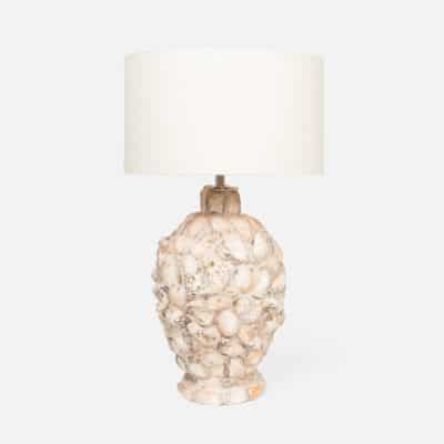 The image displays a table lamp with an oyster shell base The lamp has a white shade and is placed against a