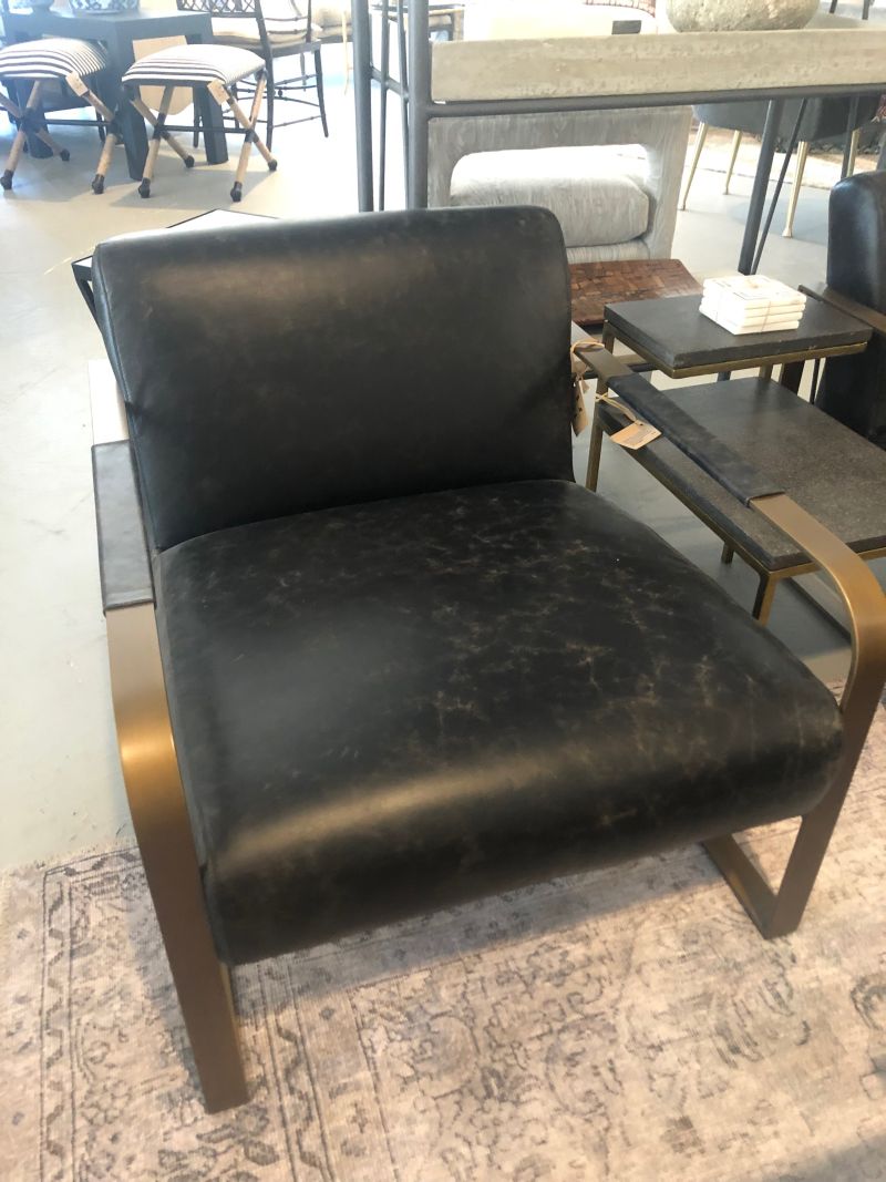 A dark brown leather armchair with a brass frame is displayed in an indoor setting.