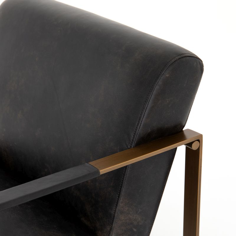 An ebony leather armchair with a brass frame, showcasing its design and material in a studio setting.