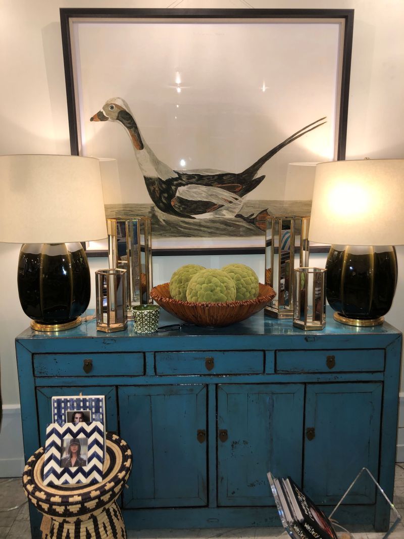 A wall hanging in a dark walnut frame depicts a seabird, surrounded by decorative items on a blue wooden cabinet.