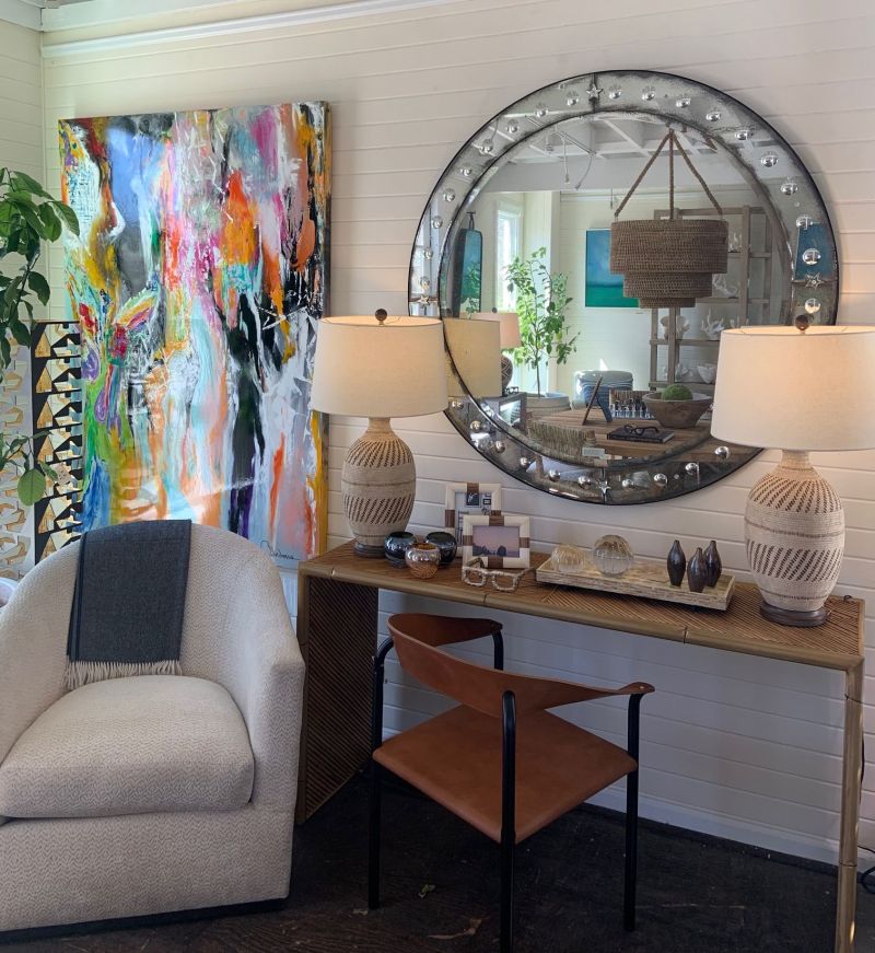 A well-lit room with a large mirror reflecting a colorful painting To the left there is a white sofa and a coffee