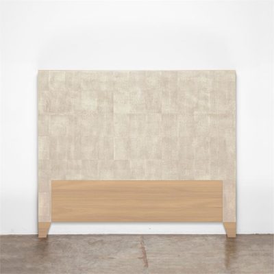 A beige faux shagreen headboard with wooden base against a white wall.