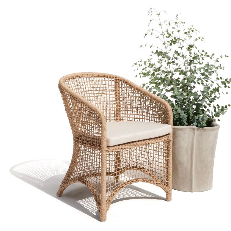 An outdoor wicker armchair with a curved frame, featuring a beige fabric upholstery, positioned beside a pot plant on a white background.