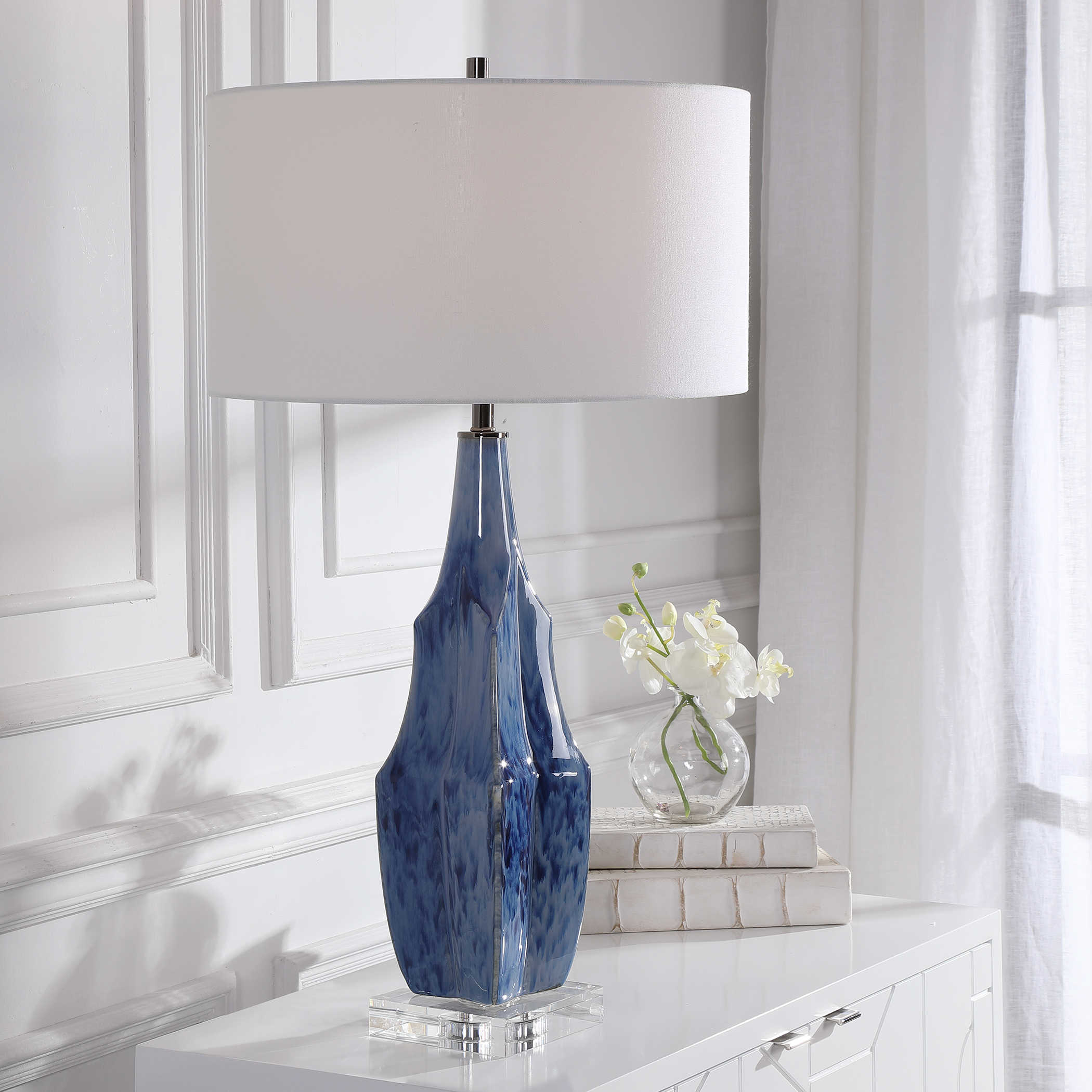 Indigo blue table lamp with a crystal base and nickel hardware sitting on a white surface next to a vase and a