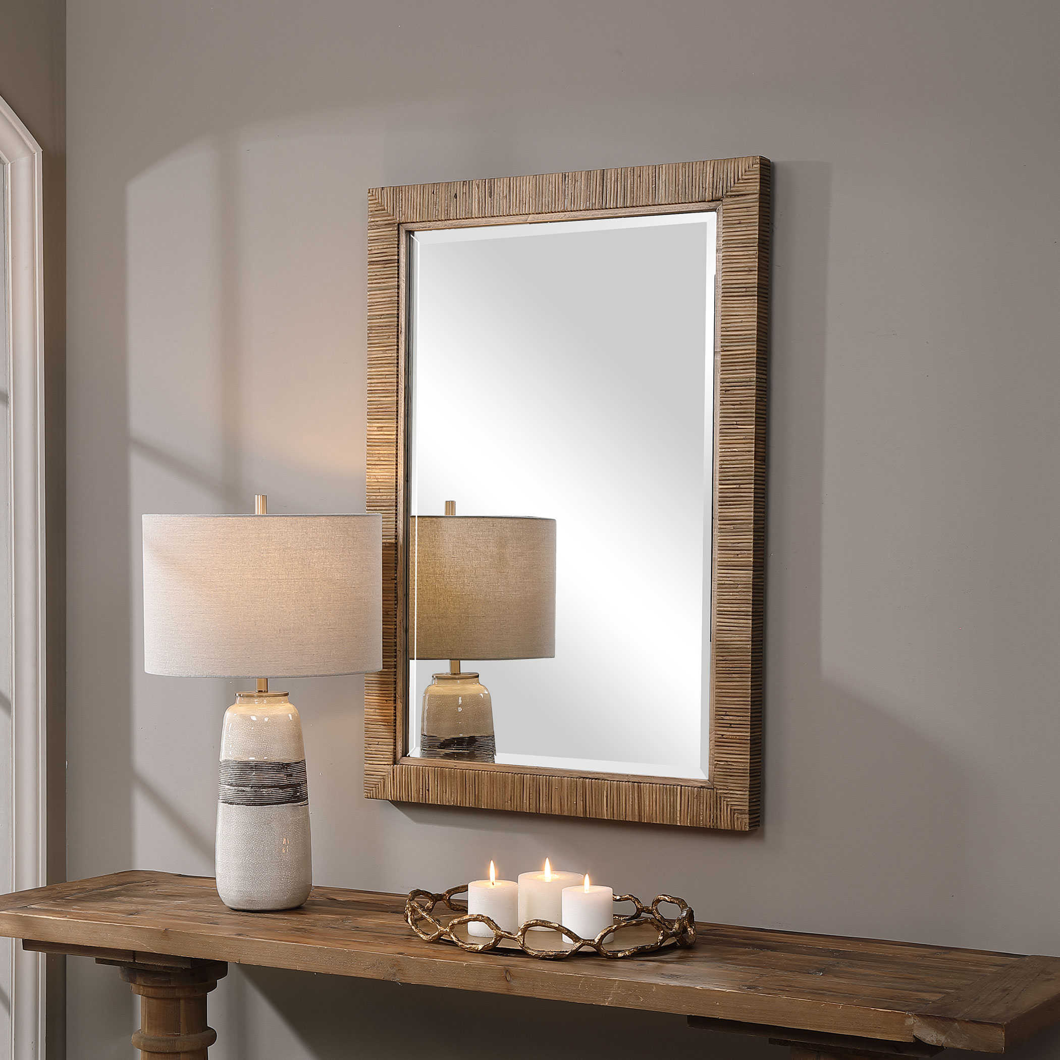 Rectangular mirror with a woven wooden frame and a beveled edge displayed on a table next to a lamp with a white